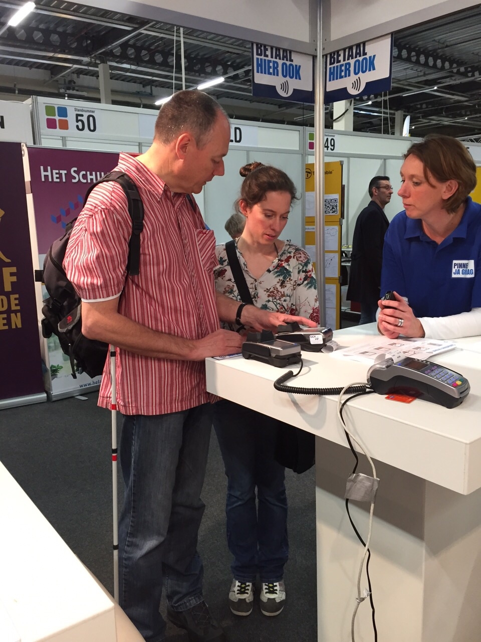 Bezoekers oefenen contactloos betalen bij een demonstratiestand op de ZieZo-beurs, met uitleg van een medewerker.