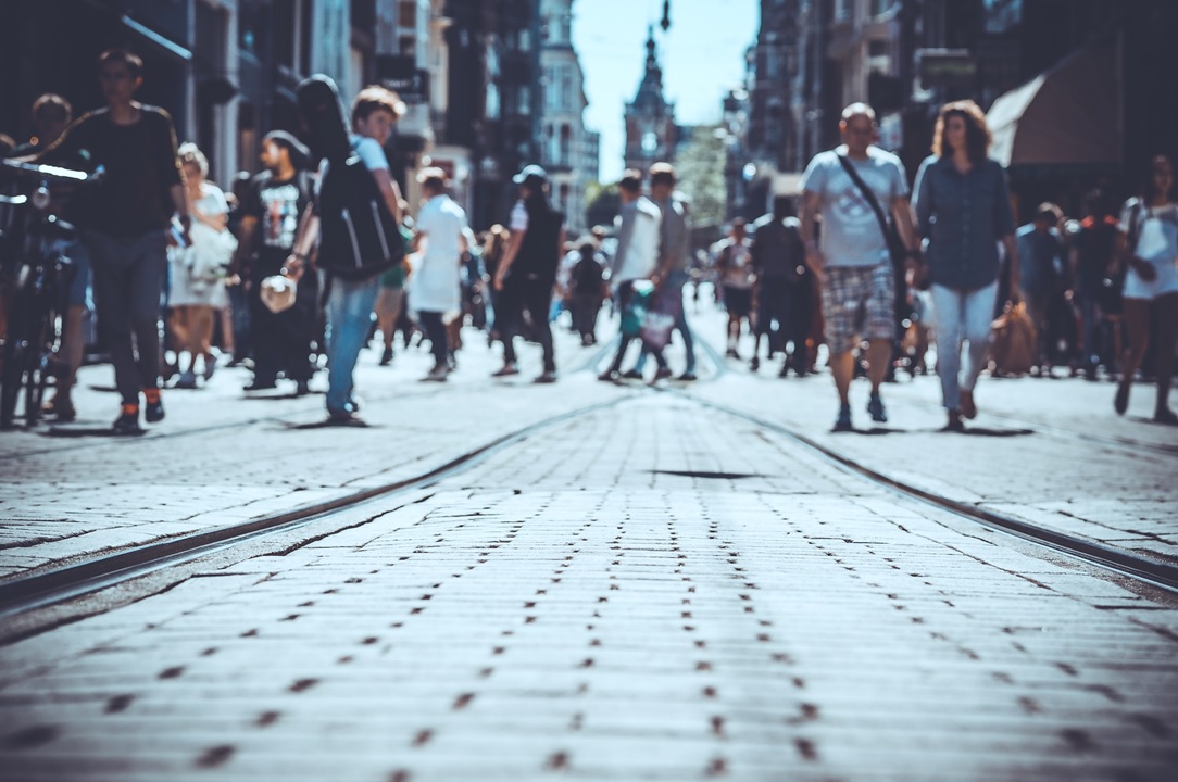 Drukke winkelstraat met voetgangers die door elkaar lopen over een geplaveide straat, wat het dagelijkse stadsleven en consumentendrukte weergeeft.