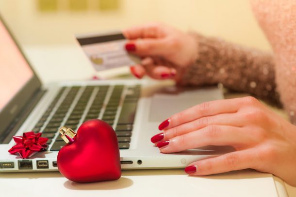 Woman making an online purchase with a credit card beside a laptop and red Christmas decorations.