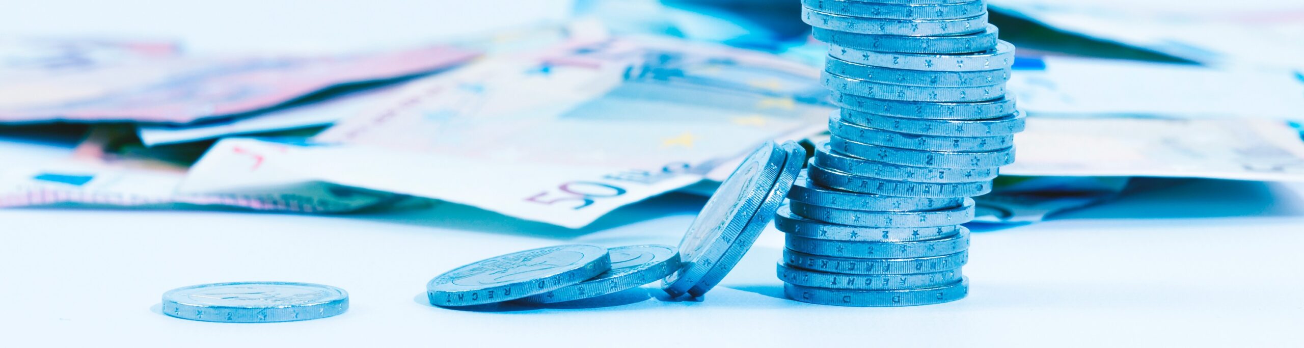 Gestapelde euromunten op een lichte ondergrond met vage eurobiljetten op de achtergrond, symbool voor contant geld en kosten.