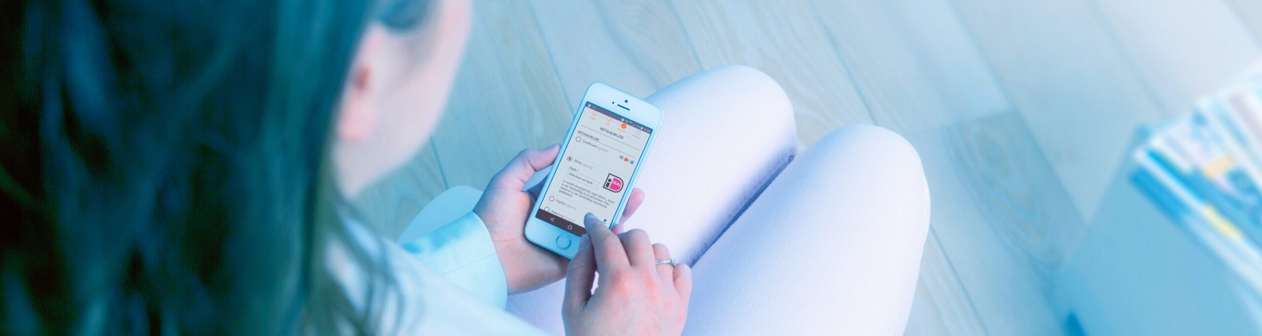 Woman chooses iDEAL as a payment method on her smartphone during an online purchase in a bright, homely environment.
