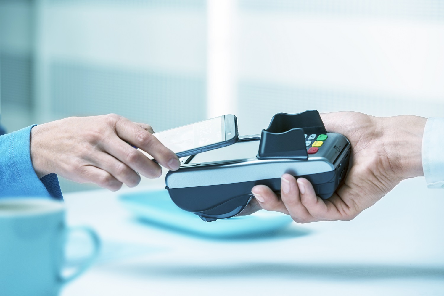 Customer holds smartphone against POS terminal for contactless payment in bright shopping environment.
