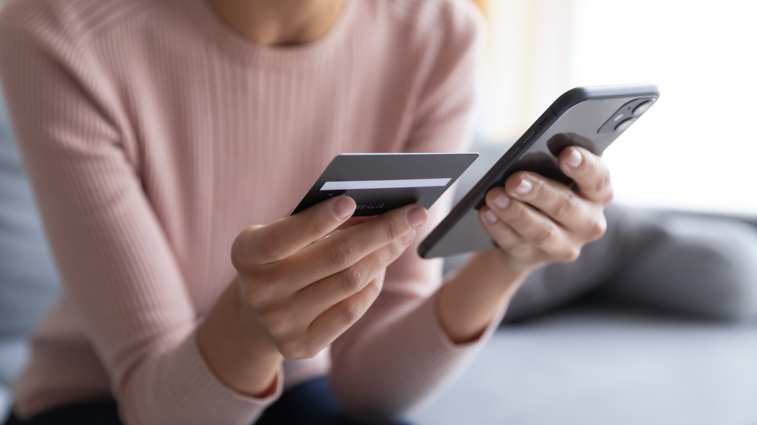 Person holds a credit card and smartphone while making an online payment in a quiet, homely environment.