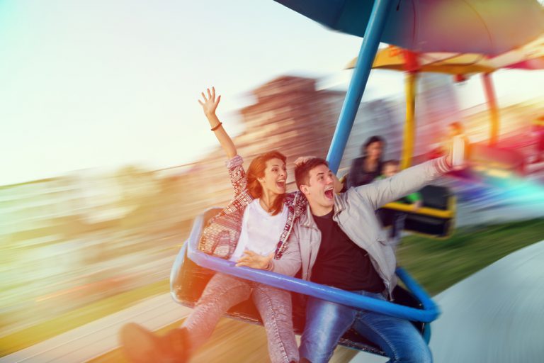Young couple smile while riding a carousel at an amusement park.