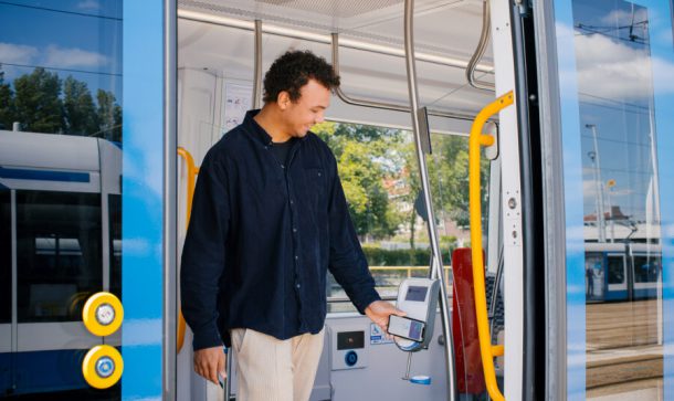 Passenger holds a smartphone to a contactless card reader while boarding a tram.