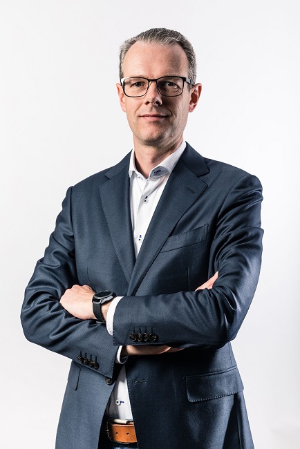 Portrait of Oscar Covers, cybersecurity analyst at the Dutch Payments Association, wearing glasses and a dark blue suit with his arms folded.