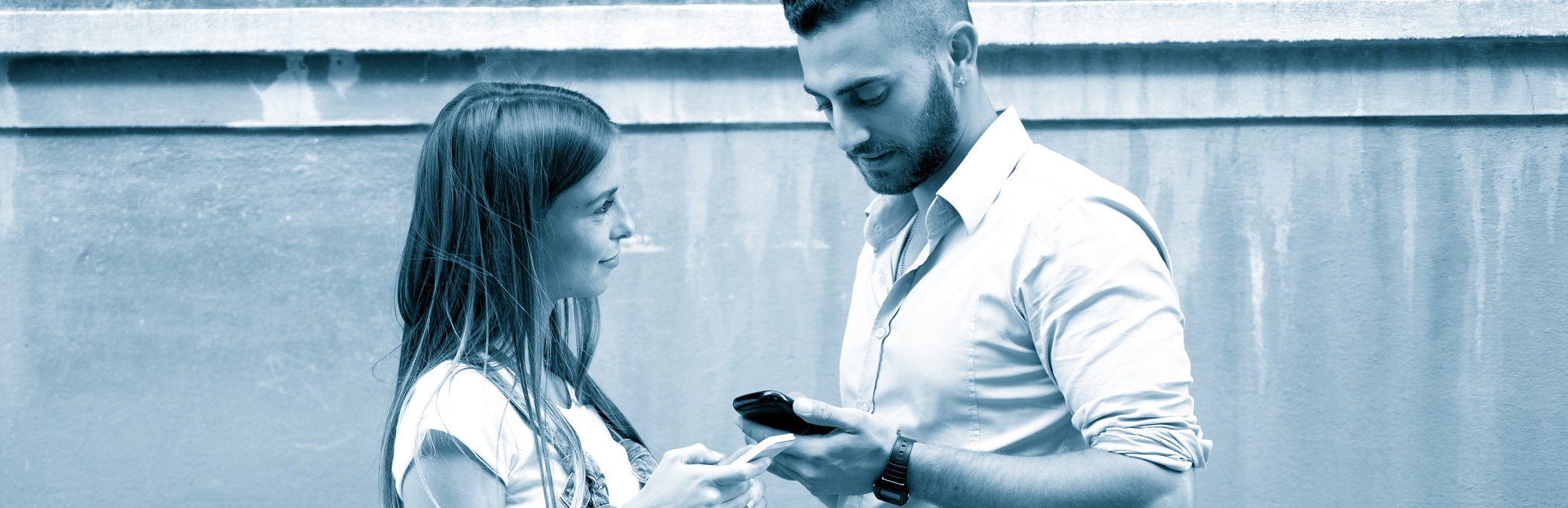 Young man and woman stand opposite each other outside and use their smartphones for a request-to-pay.