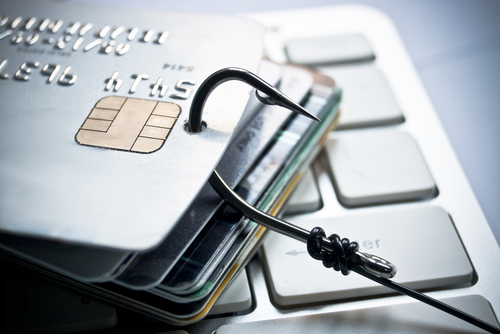 Stack of payment cards on computer keyboard with fishing hook through it, as a metaphor for phishing and online payment fraud.