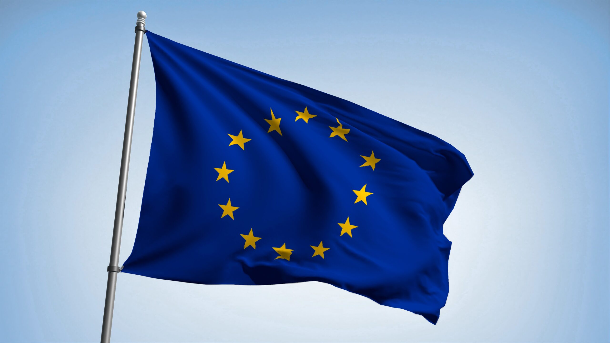 Wapperende Europese vlag met gele sterrenkring op blauwe achtergrond tegen heldere hemel, symbool voor de Europese Unie.
