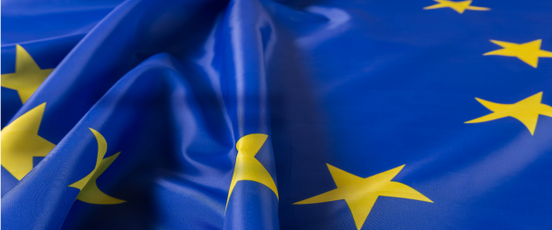 Golvende vlag van de Europese Unie met gele sterren op blauwe achtergrond, symbool voor Europese samenwerking en regelgeving.