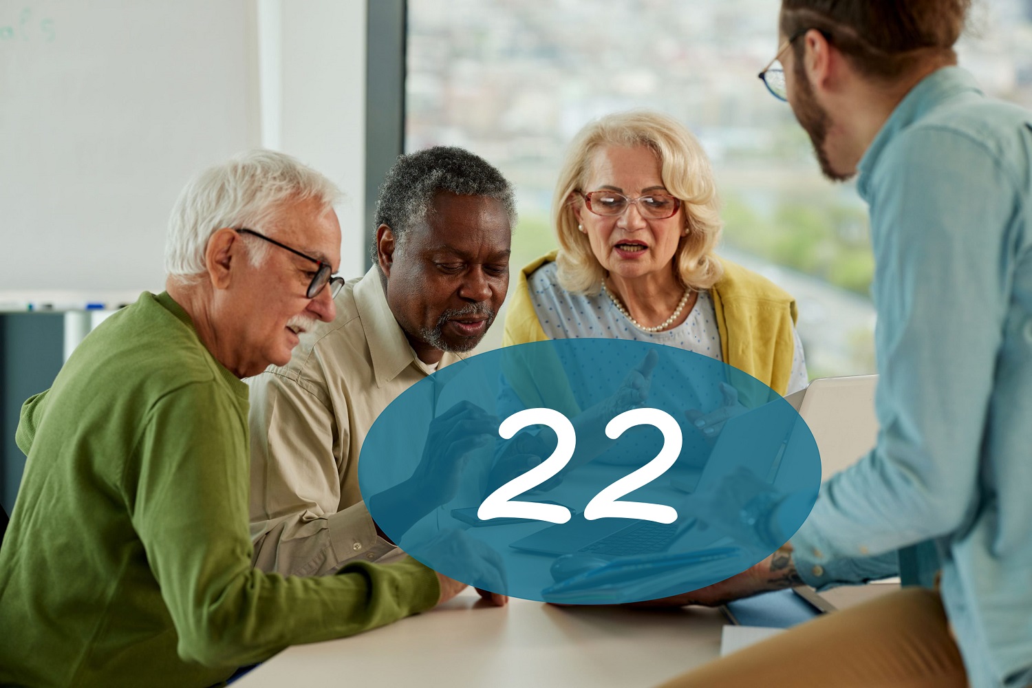 Group of older people getting explanation from younger man near laptop and smartphone during digital skills training and big number 22 in blue circle.
