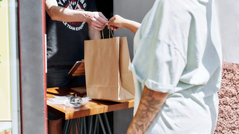 Shop employee hands an online order to a customer at a physical store.