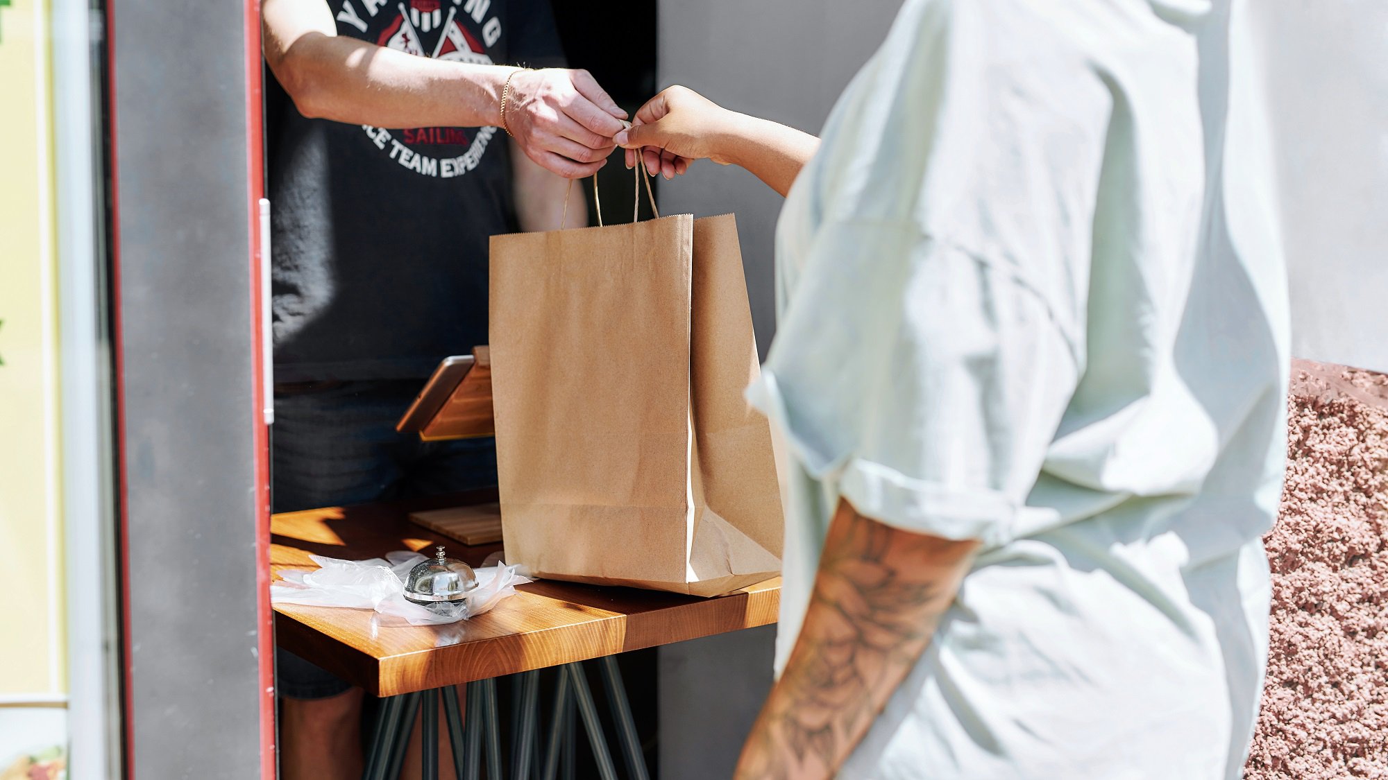 An employee hands a paper pickup bag to a customer at a counter to complete an order.
