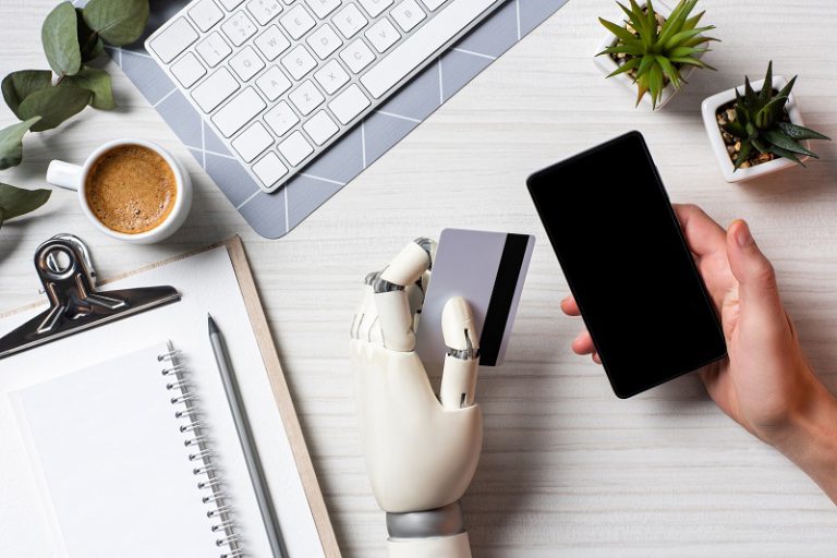 Human hand holds a smartphone while a robot hand holds a payment card, symbolising digital payments and automation.