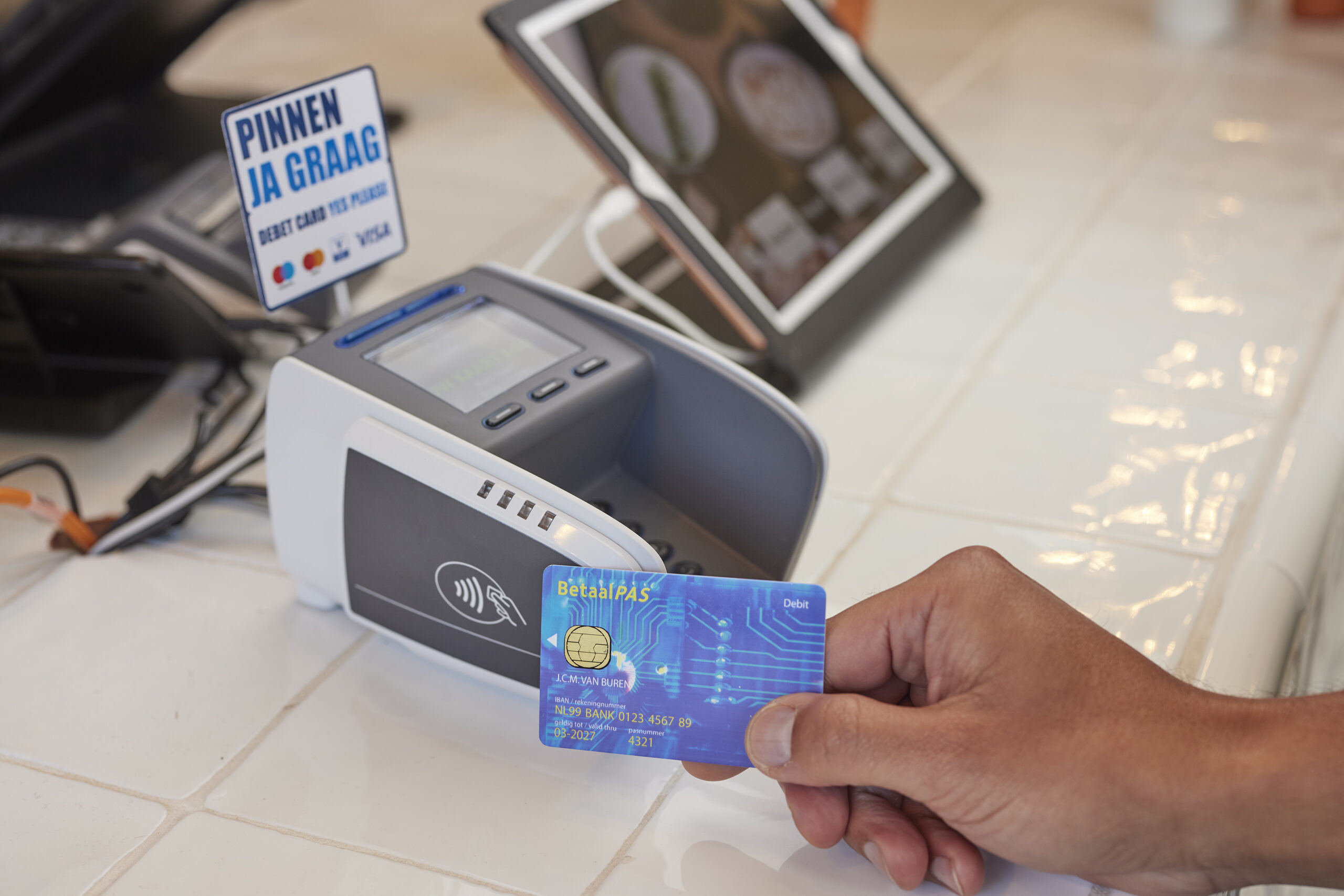 Hand houdt een betaalpas tegen een pinterminal voor een contactloze pintransactie aan de winkelbalie.