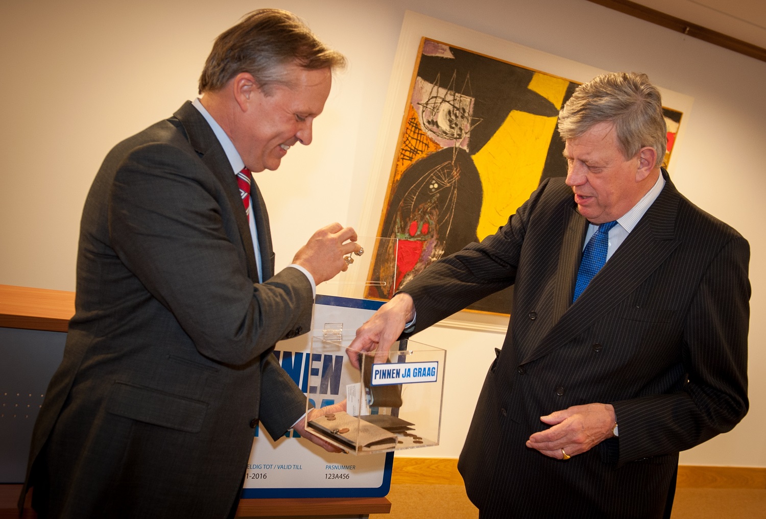 Two men in suits put cash in a transparent collection box with the inscription “pay with debit cards yes please”, during a public meeting about payments.