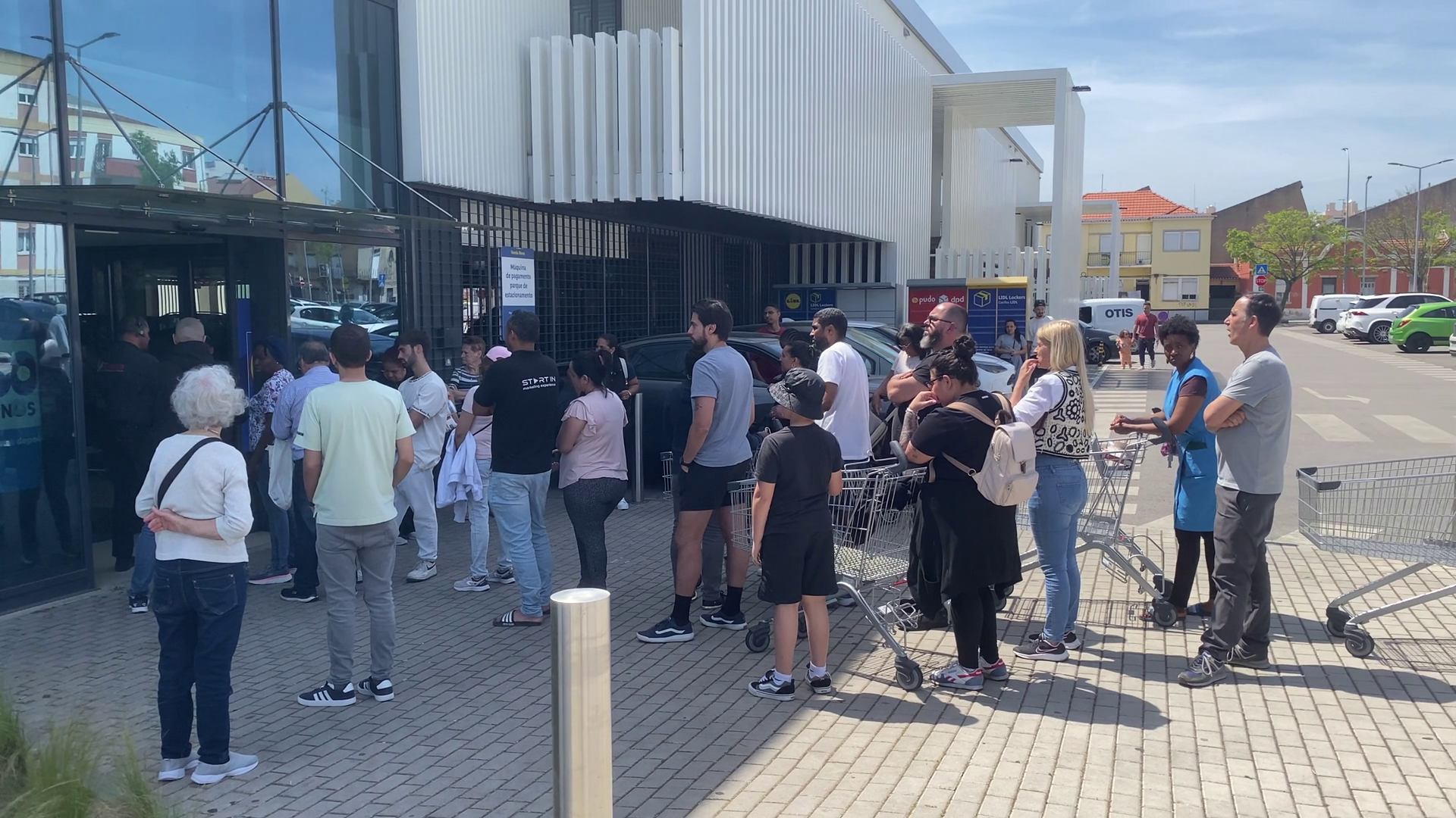 Mensen staan in een lange rij met winkelwagens bij de ingang van een supermarkt en wachten om naar binnen te gaan.