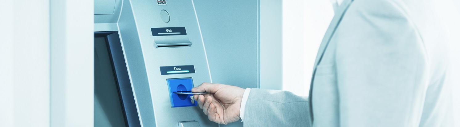 Persoon steekt een betaalpas in een moderne geldautomaat in een lichte, zakelijke omgeving.