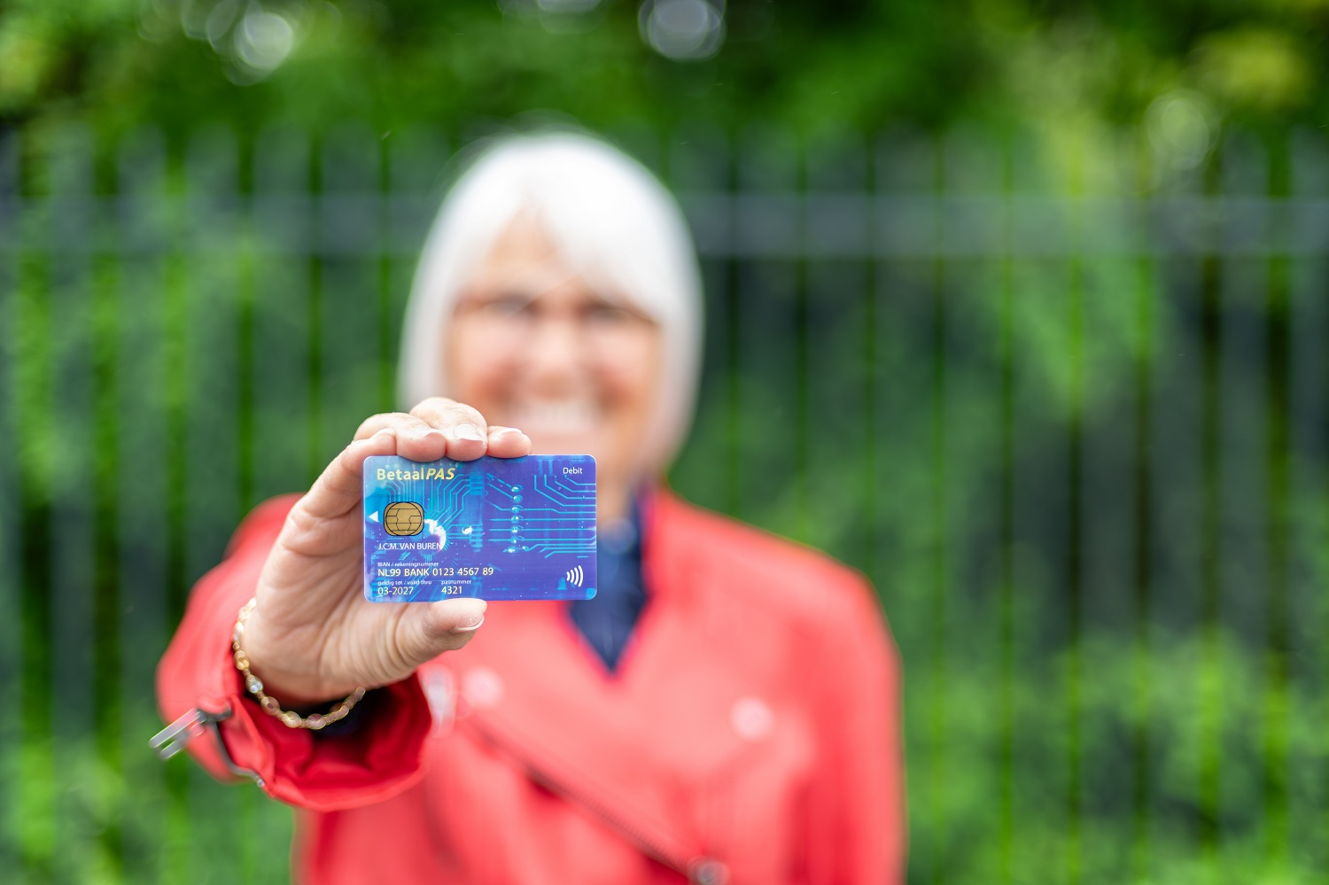 Oudere vrouw houdt een betaalpas duidelijk naar voren in een groene buitenomgeving, waarmee zij laat zien dat zij eenvoudig en zelfstandig kan betalen.