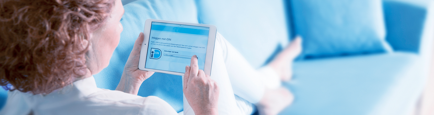 Vrouw zit ontspannen op bank en logt via iDIN in op tablet, met helder blauw inlogscherm op de voorgrond.