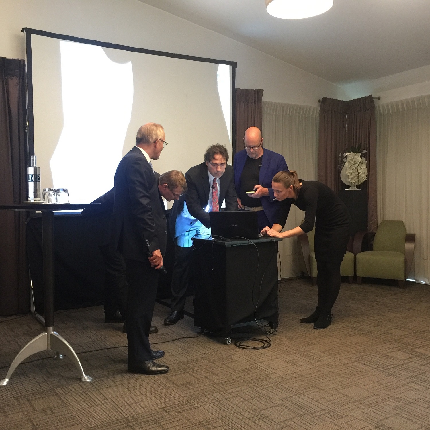 Bestuurders en medewerker buigen zich in conferentieruimte over laptop om presentatie over betalingsverkeer technisch gereed te maken.