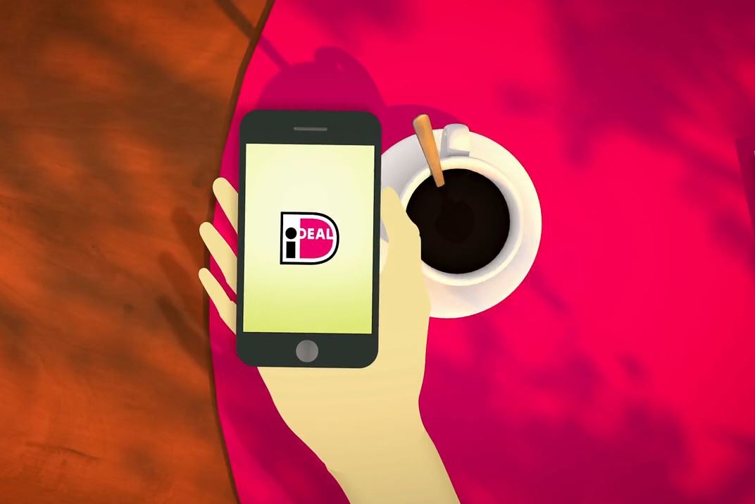 Illustratie van hand met smartphone met iDEAL-logo op tafel, naast een kop koffie op felroze tafelblad.