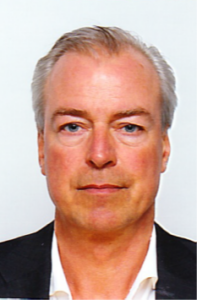 Neutrale pasfoto van een man met grijs haar in donker colbert en wit overhemd, recht in de camera tegen een lichte achtergrond.