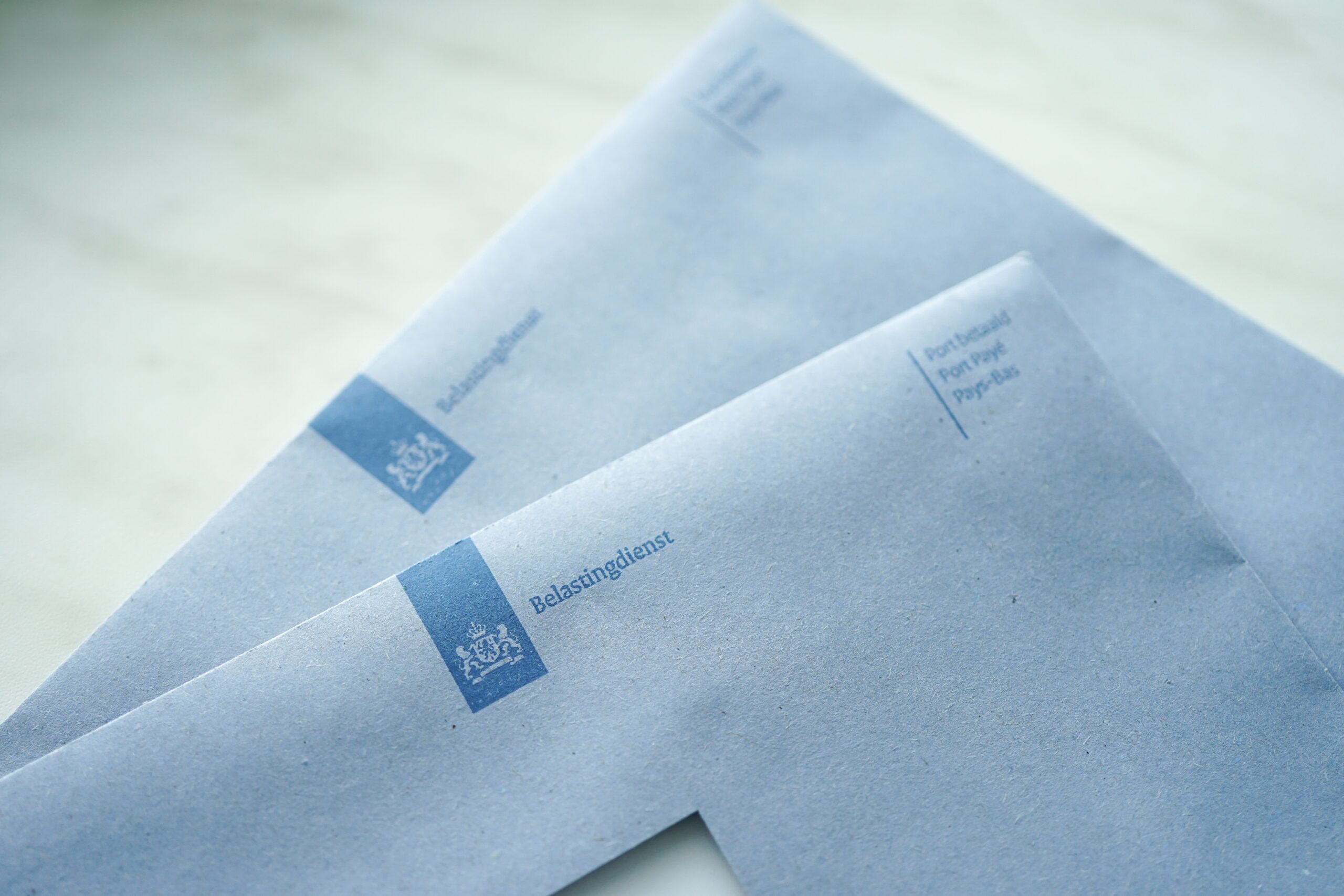 Blauwe brieven van de Belastingdienst liggen in zacht licht, met zichtbaar logo en postadres.