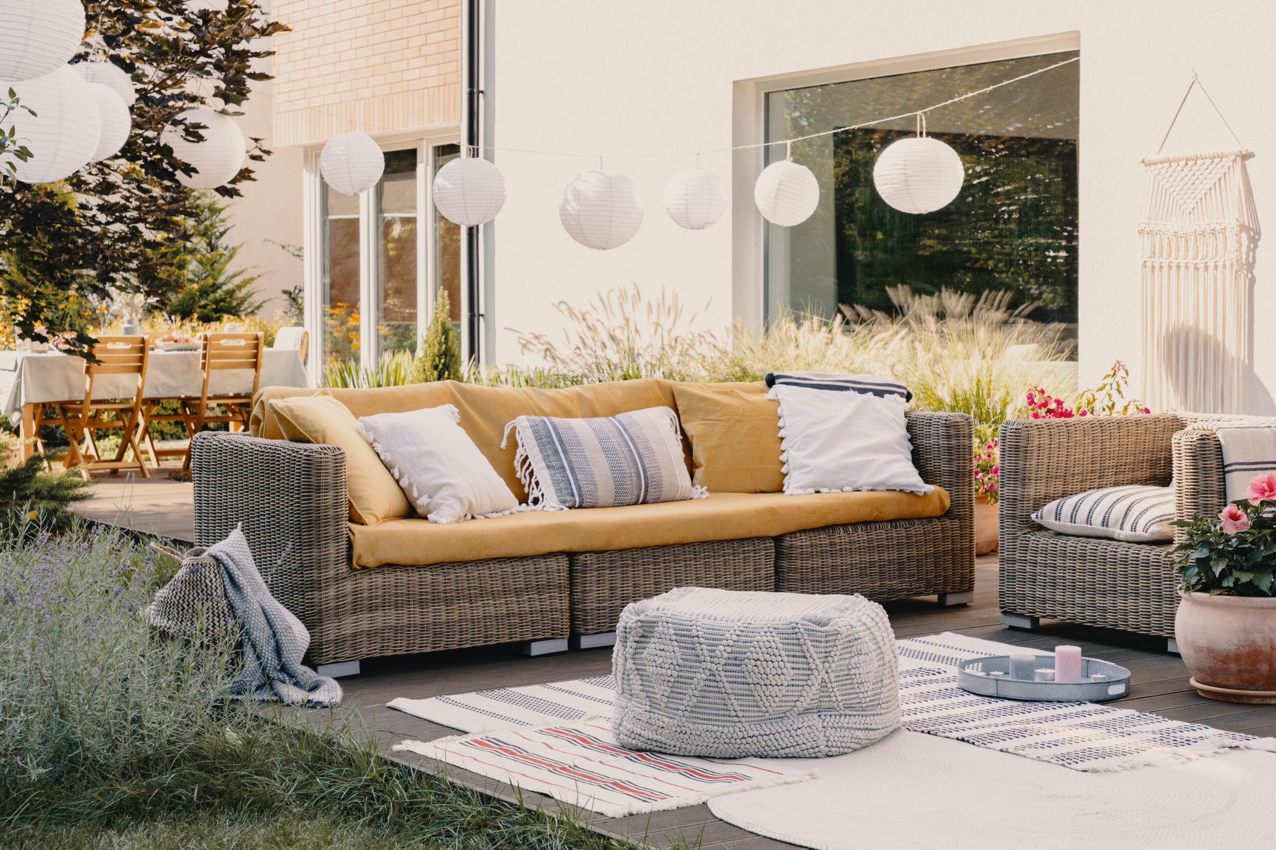 Sfeervol ingericht terras met rotan loungezetels, zachte kussens en tuinverlichting bij een moderne woning.